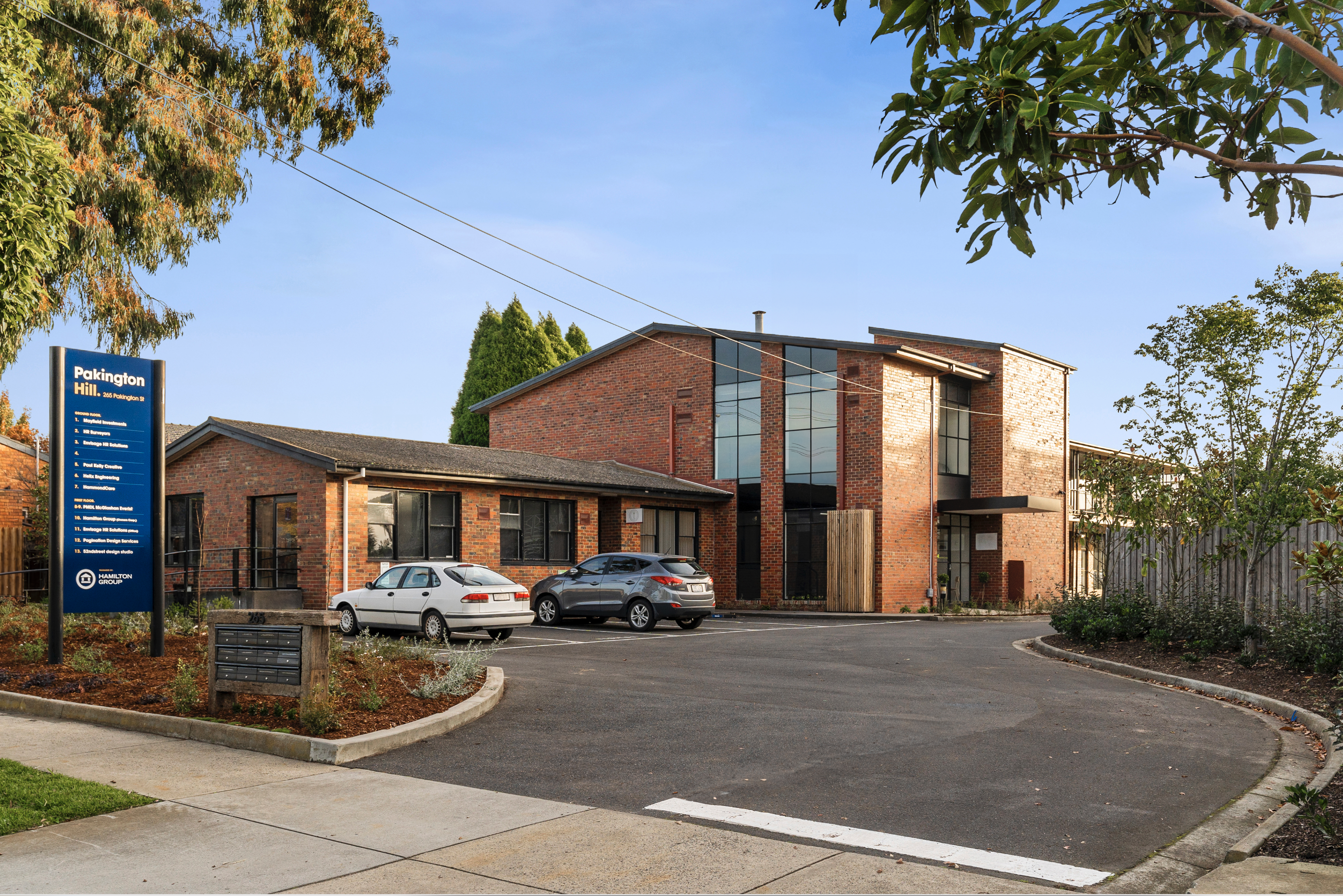Large wash bricked facade featuring multiple black windows, road way runs up towards the building with a sign on the left side stating "Pakington Hill" and a directory, Building leased by Hamilton Property Group